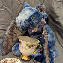 Blue and grey dragon sipping from a teacup with pansies on it